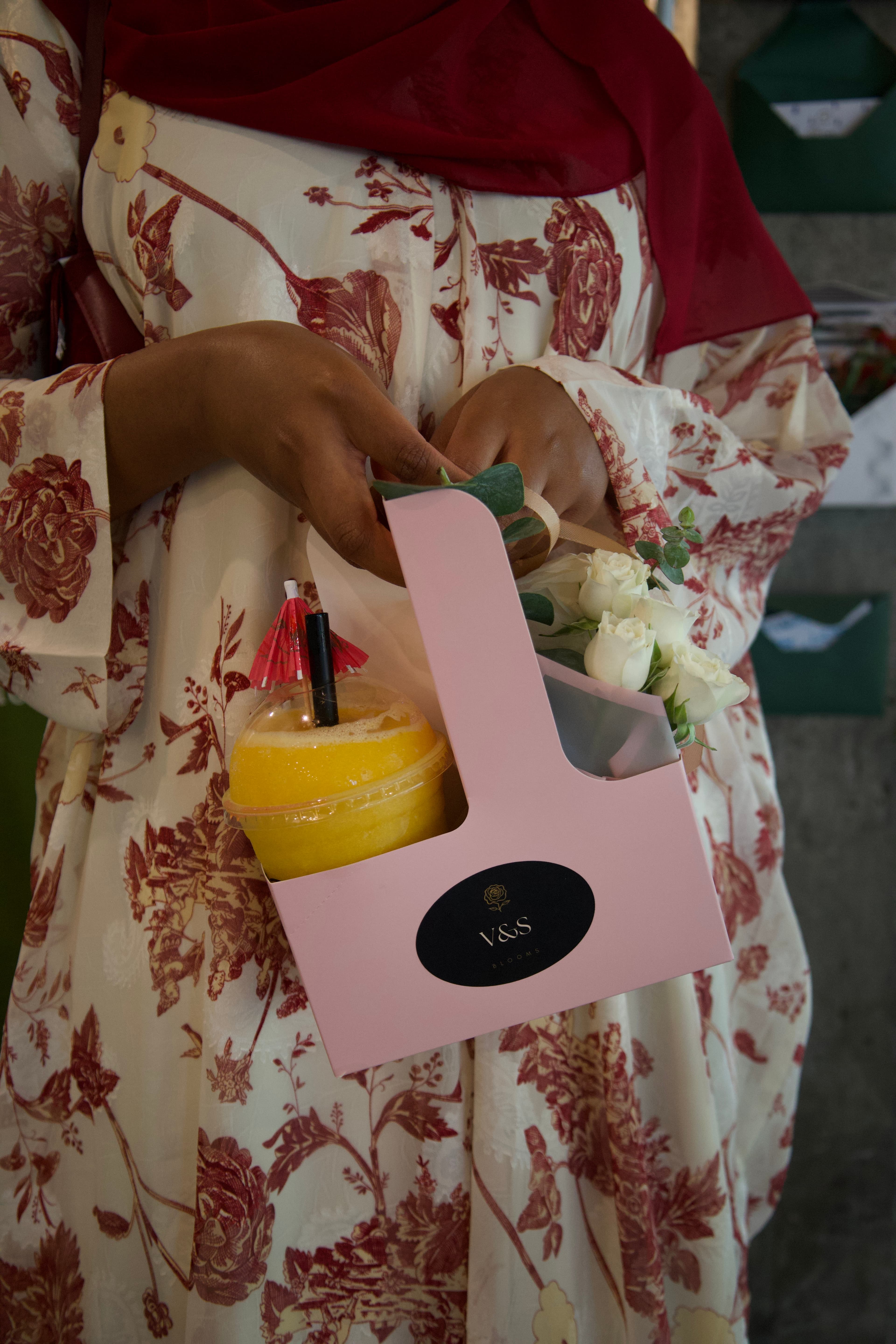 Guest holding a drink and a bouquet of white roses at an event, photographed by ShuhraBilNoor