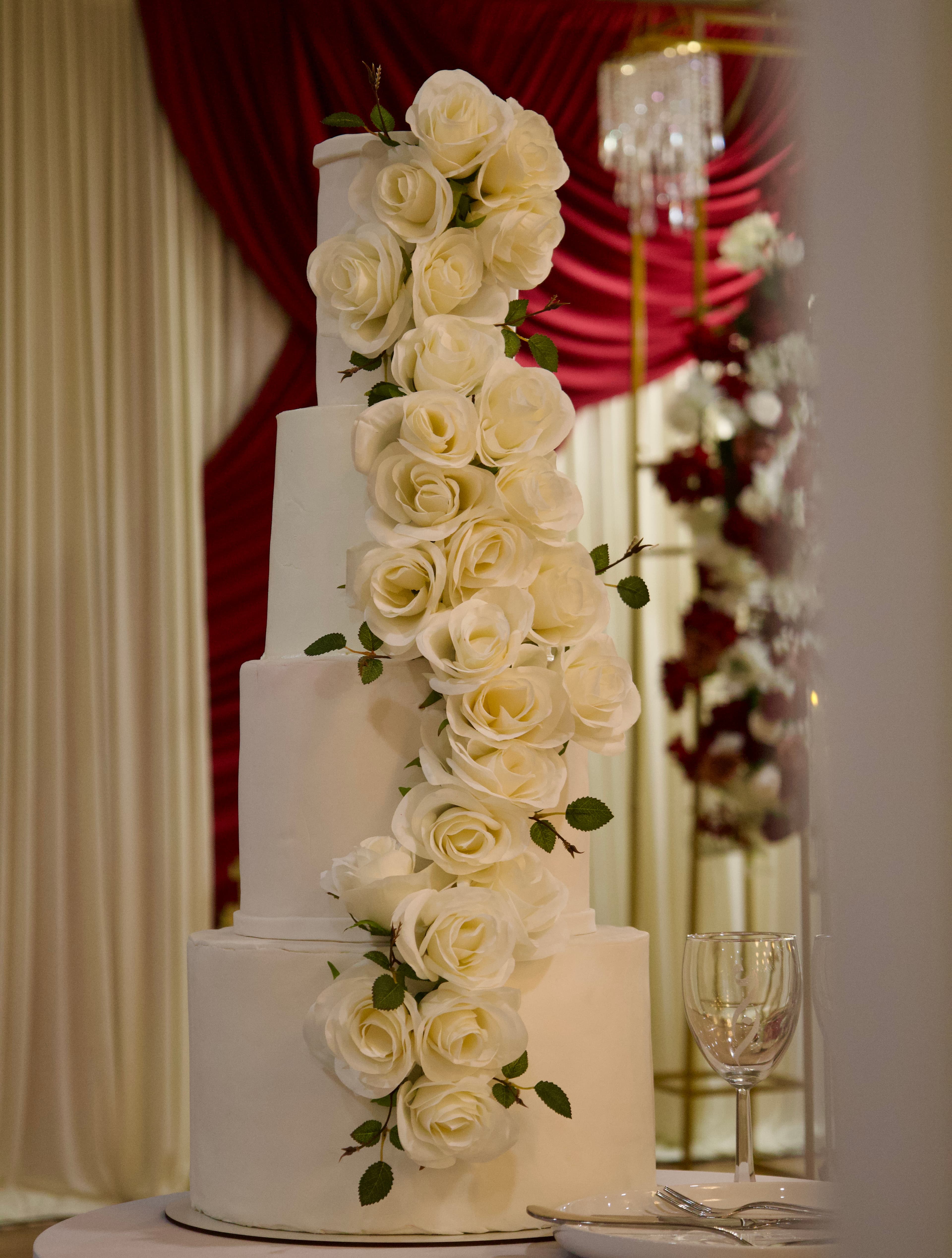 Five-tier white wedding cake decorated with cascading ivory roses, photographed by ShuhraBilNoor