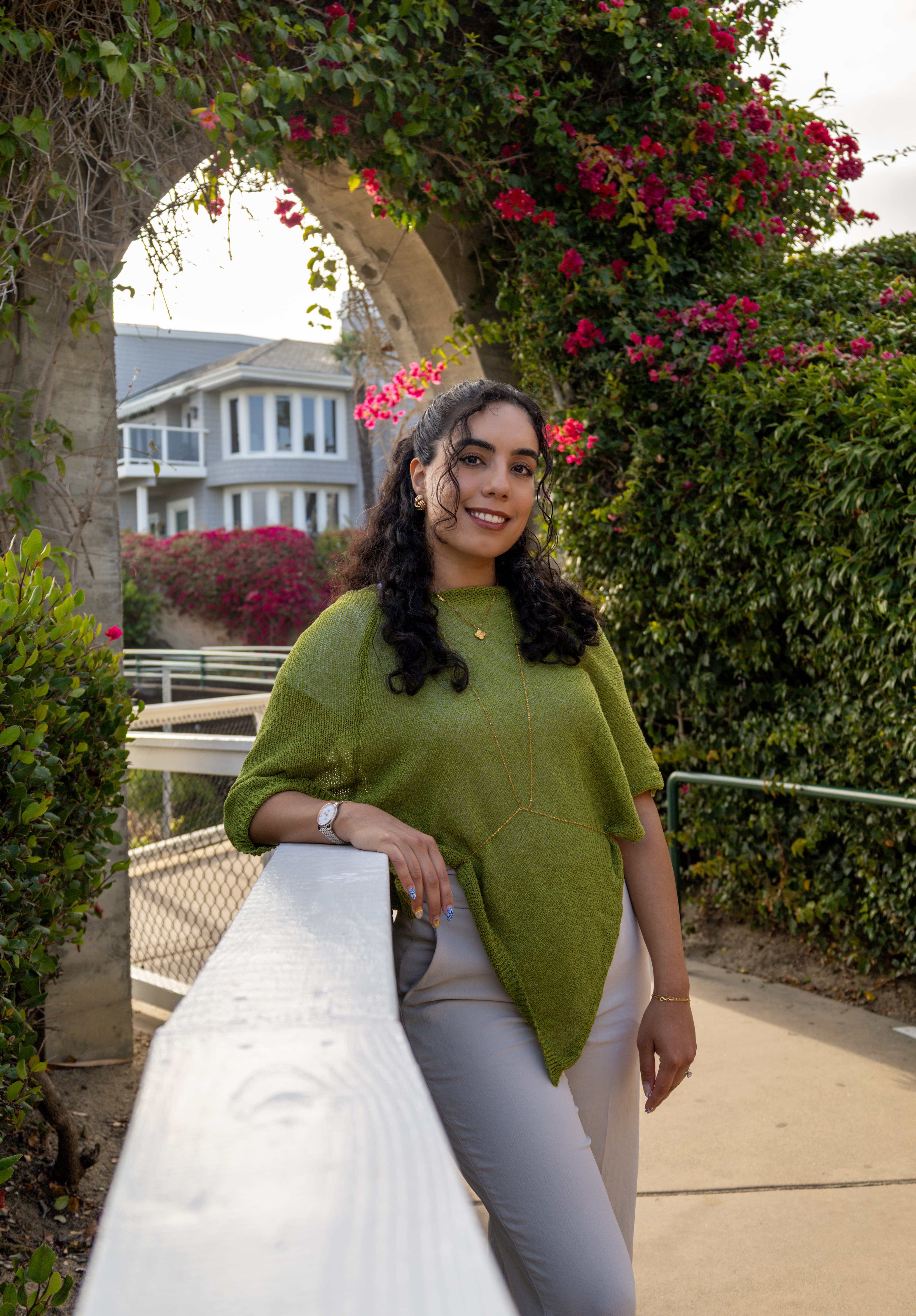 Portrait photographed by ShuhraBilNoor, client in a green sweater leaning on a railing under a flowering archway