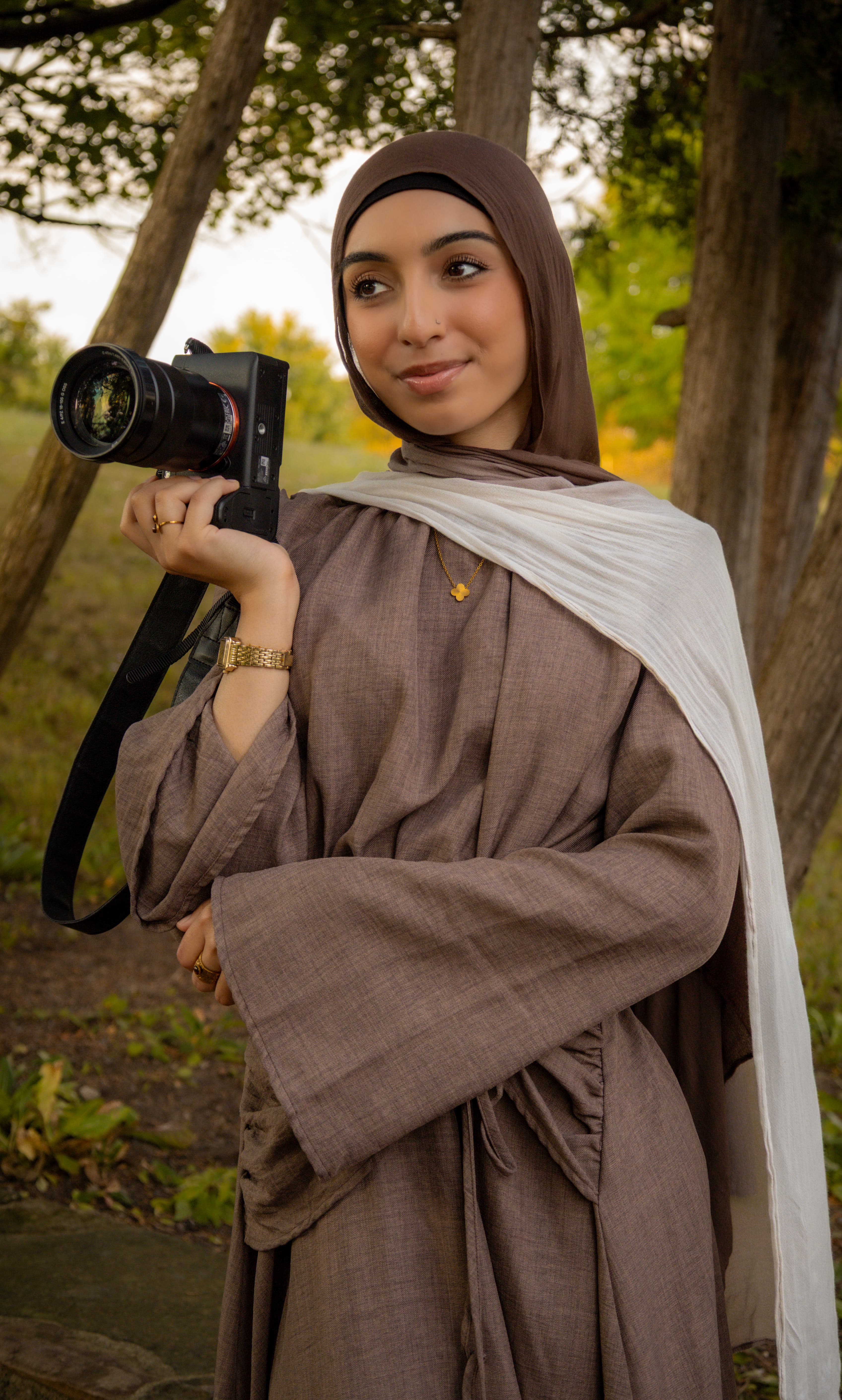 Shahra, ShuhraBilNoor Photography's photographer, smiling while holding her camera outdoors